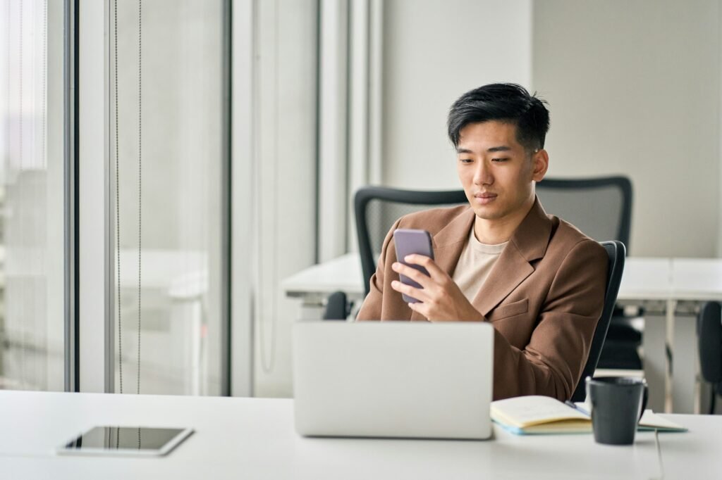 Young busy smiling Asian business man using phone in corporate office.